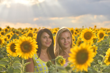 Fototapeta na wymiar Two beautiful girls feeling free in a lovely sunflower field at sunset