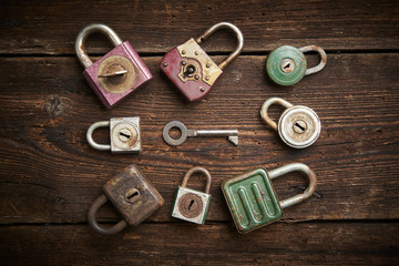 Group of old rusty padlocks with pile of keys on brown wooden table

