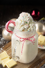 Hot white chocolate with whipped cream and candy cane in a xmas decoration on dark wooden background. Winter Christmas time.