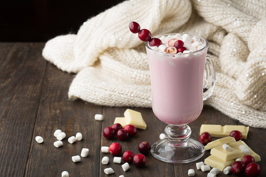 Hot white chocolate with cranberry, knitted blanket and marshmallows on dark wooden background. Winter Christmas time.