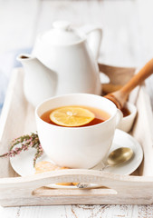 Tray with cup of hot black tea, lemon and honey on white rustic wooden table. Breakfast concept.