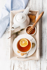 Tray with cup of hot black tea, lemon and honey on white rustic wooden table. Breakfast concept. Top view
