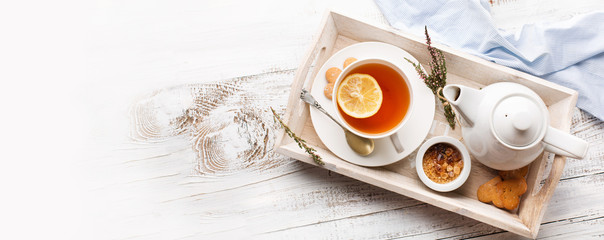 Tray with cup of hot black tea, lemon and honey on white rustic wooden background. Breakfast...