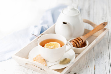 Tray with cup of hot black tea, lemon and honey on white rustic wooden background. Breakfast concept.