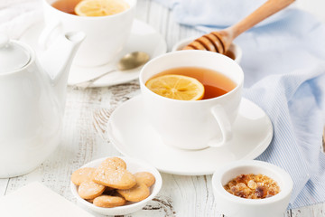 Cups of hot black tea, lemon and honey on white rustic wooden background. Breakfast concept. Selective focus