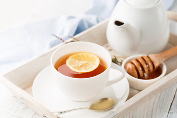 Tray with cup of hot black tea, lemon and honey on white rustic wooden background. Breakfast concept. Selective focus