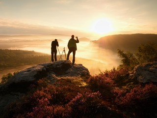  Photographers stay on cliff and takes photos. Dreamy fogy landscape, orange mist