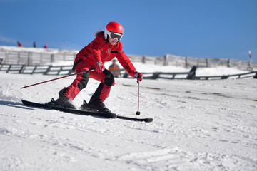 Woman in red suit skiing downhill with blue sky in background
