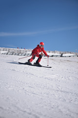 Woman in red suit skiing downhill with blue sky in background