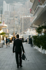 Look from behind at tall man in black suit walking along the str