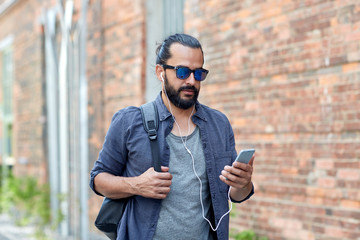 man with earphones and smartphone walking in city