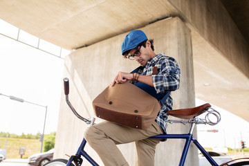hipster man with bicycle looking something in bag