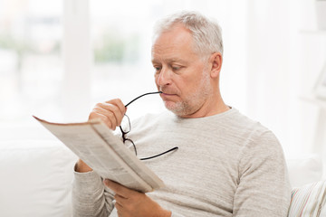 senior man in glasses reading newspaper at home
