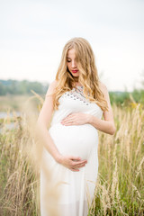Fototapeta na wymiar Yonge pregnant woman in a white dress with long blond hair in tall grass