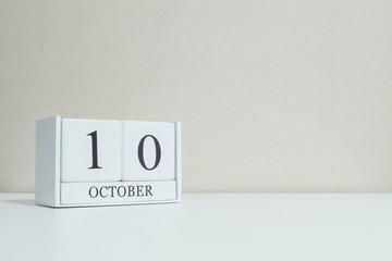 Closeup white wooden calendar with black 10 october word on blurred white wood desk and cream color wallpaper in room textured background with copy space , view another more date in my portfolio