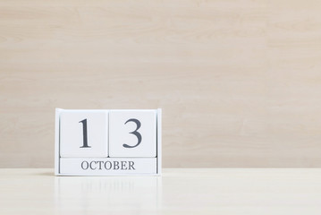Closeup surface white wooden calendar with black 13 october word on blurred brown wood desk and wood wall textured background with copy space , view another more date in my portfolio