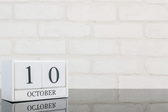 Closeup white wooden calendar with black 10 october word on black glass table and white brick wall textured background with copy space , view another more date in my portfolio