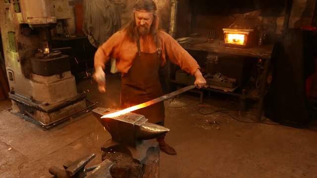 Senior blacksmith forging the molten metal on the anvil in smithy