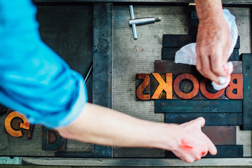  Detail of hands using letterpress machine in book arts workshop, overhead view