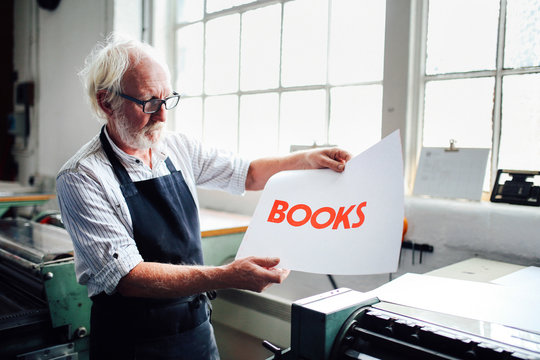 Senior craftsman/technician holding up letterpress print in book arts workshop