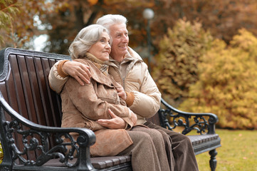 Happy elderly couple sitting on a bench in autumn park