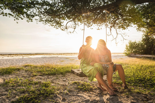 Two women sitting on beach tree swing at sunset, Gili Trawangan, Lombok, Indonesia