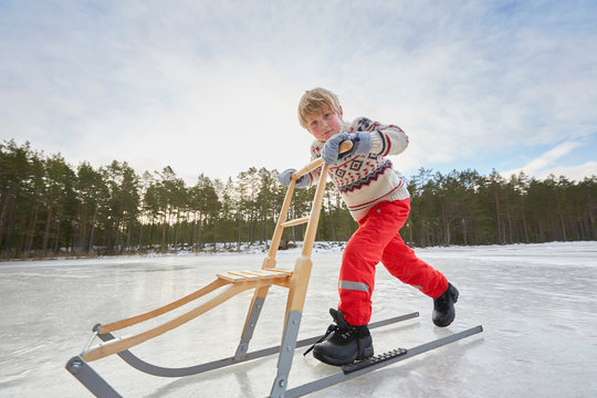 Boy pushing kicksled across frozen lake, Gavle, Sweden