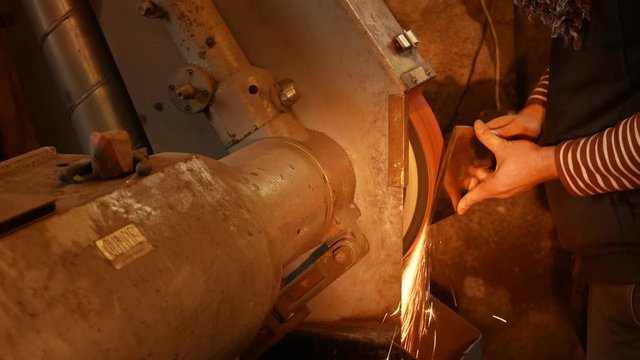 The blacksmith sharpening an ax on electrical grinder