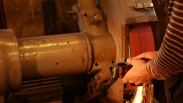 The blacksmith sharpening an ax on electrical grinder