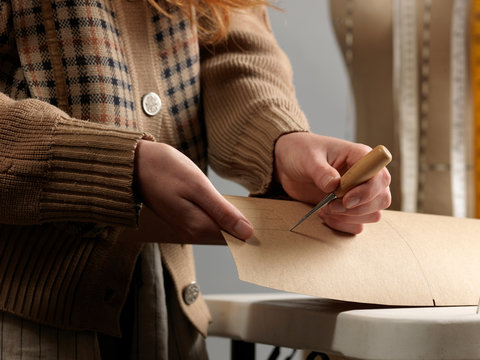 Cropped close up of young female fashion designer piercing dressmaker's pattern