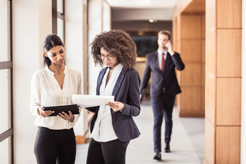 Young businesswomen reading paperwork in office corridor