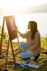 young artist draws a seascape at sunset