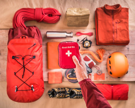 Overhead view of man's hand holding first aid kit above climbing equipment packing with climbing helmet, rucksack and climbing ropes