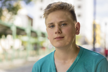 Handsome young blond teenage boy looking at the camera with a quiet friendly smile against a high key urban backdrop, head and shoulders portrait