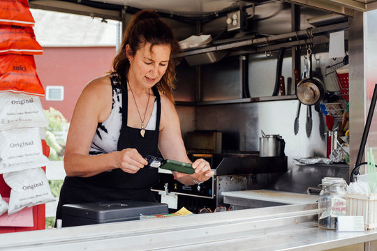 Woman using smartphone card reader for payment at food stall trailer