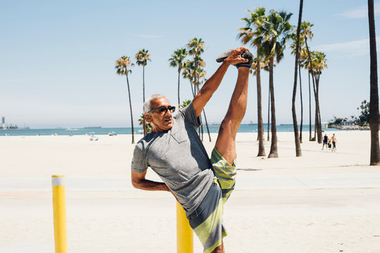 Senior man, exercising on beach, stretching leg, Long Beach, California, USA