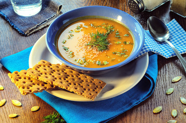 Pumpkin cream-soup. Pumpkin cream-soup. Hot pumpkin soup with toasted sesame seeds in a blue bowl on a wooden table. Still life with a bowl of soup, spoon, pumpkin seeds and slices of bread