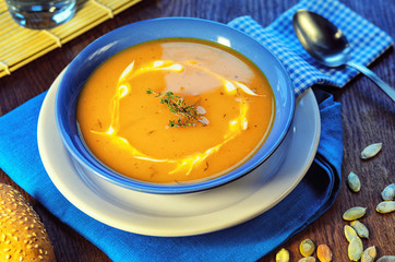 Pumpkin cream-soup. Hot pumpkin soup with sour cream and pumpkin seeds in a blue bowl on a wooden table. Healthy food still life