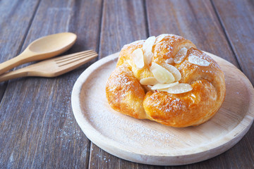 Close up fresh croissant with almonds on wooden plate.