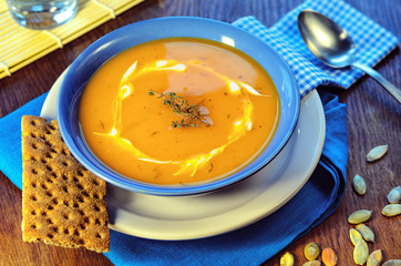 Pumpkin cream-soup. Hot pumpkin soup with sour cream and pumpkin seeds in a blue bowl on a wooden table. Healthy food still life