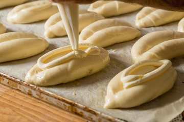 Fototapeta na wymiar Raw sweet yeast dough on a baking sheet, filling buns cheese. Preparation for baking. The concept of chefs and baking.