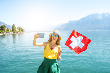 Young female traveler with swiss flag making selfie photo on Geneva lake background