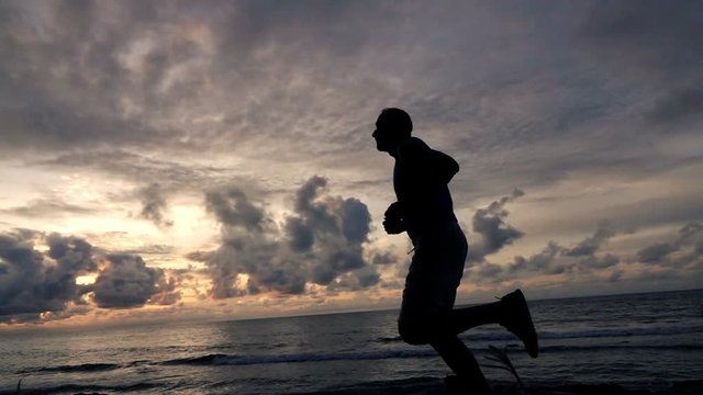 Young man jogging on beach during sunset, super slow motion 240fps
