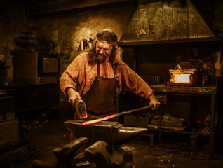 Senior blacksmith forging the molten metal on the anvil in smithy
