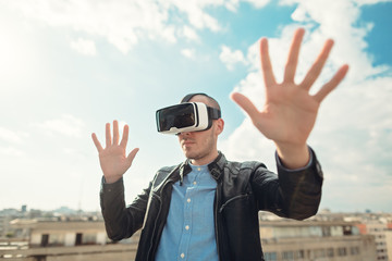 Excited young man using a pair of VR glasses above the city with the blue sky background amazed by...
