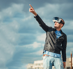 Excited young man using a pair of VR glasses above the city with the blue sky background amazed by...