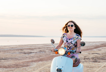 Fototapeta na wymiar Young pretty woman with tattoo riding a bike and enjoing the sunset at the seaside