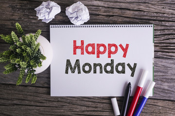 Notepad and green plant on wooden background with Happy Monday w