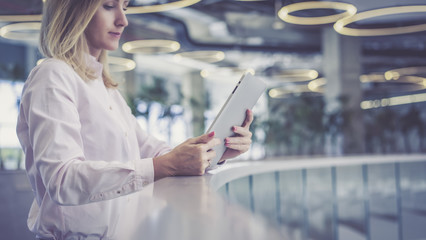 Side view, of a girl with blonde hair in a light pink shirt standing and holding a tablet...