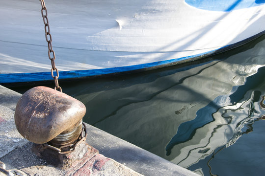 Chain tied on a bollard. Mooring rope wrapped around the cleat on sea background. Metal capstan in harbor for the mooring of yachts and boats.